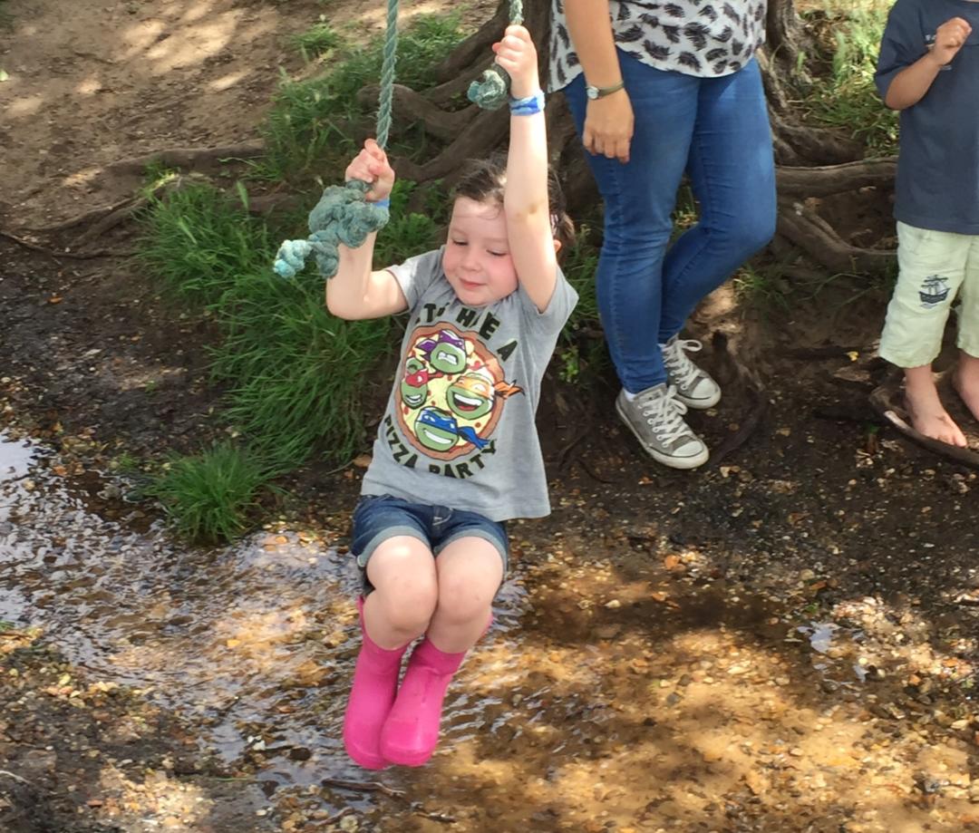 Girl swinging on rope over stream