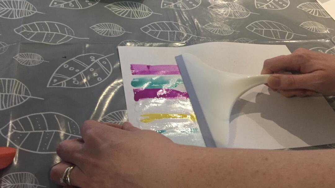 Use the squeegee to spread the paint across the paper