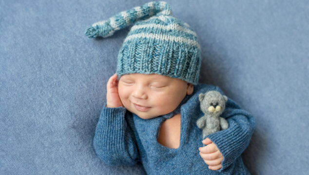 smiling sleeping newborn in blue suit and hat with toy