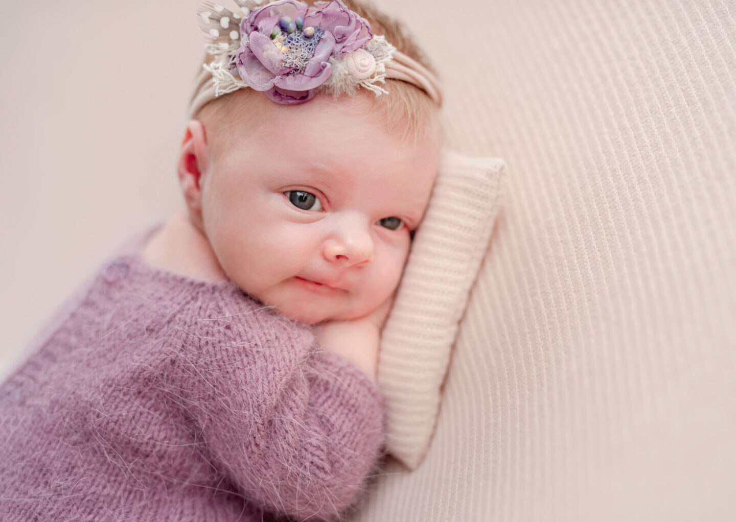 Awake newborn girl with purple flower hairband