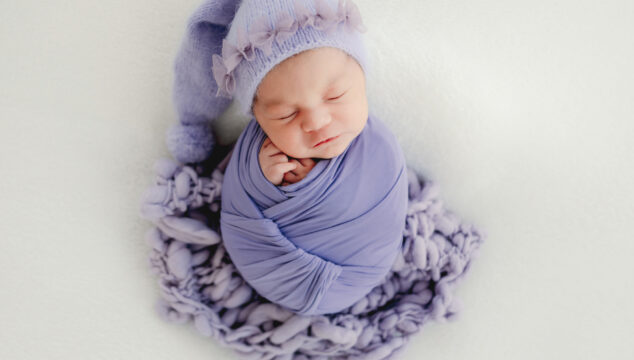 Newborn baby girl wrapped in Lilac blanket, wearing lilac hat
