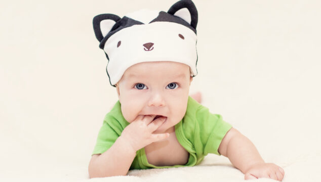 Baby on tummy in green baby grow wearing a hat with ears