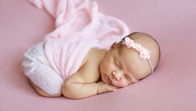 New born baby wearing a pink head band and tutu.