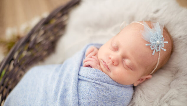 Baby girl wrapped in blue blanket asleep in basket