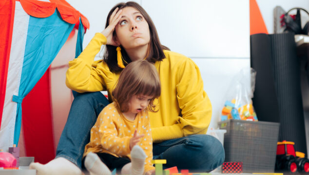 Mum sitting on the floor looking bored while child plays